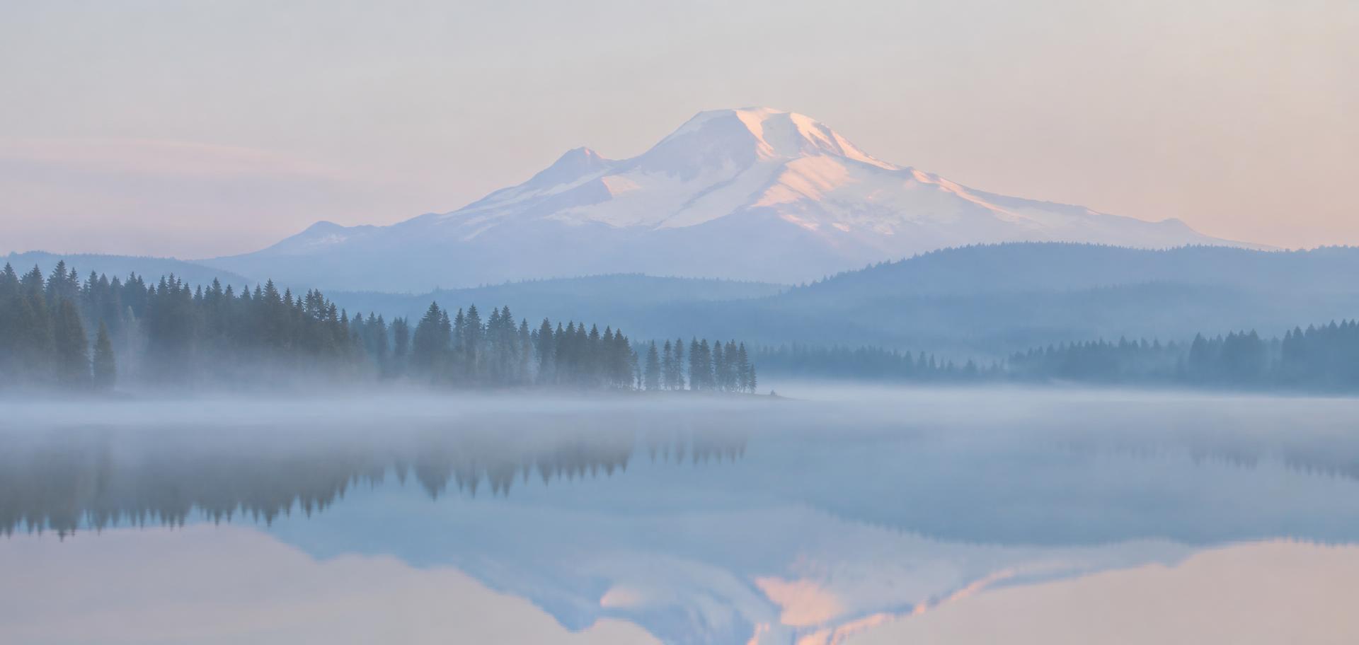 Misty Cascade volcano reflected in a calm lake at sunrise